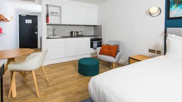 Una habitación de hotel moderna con una cama, un escritorio, una silla, una pequeña cocina y un pouf redondo.