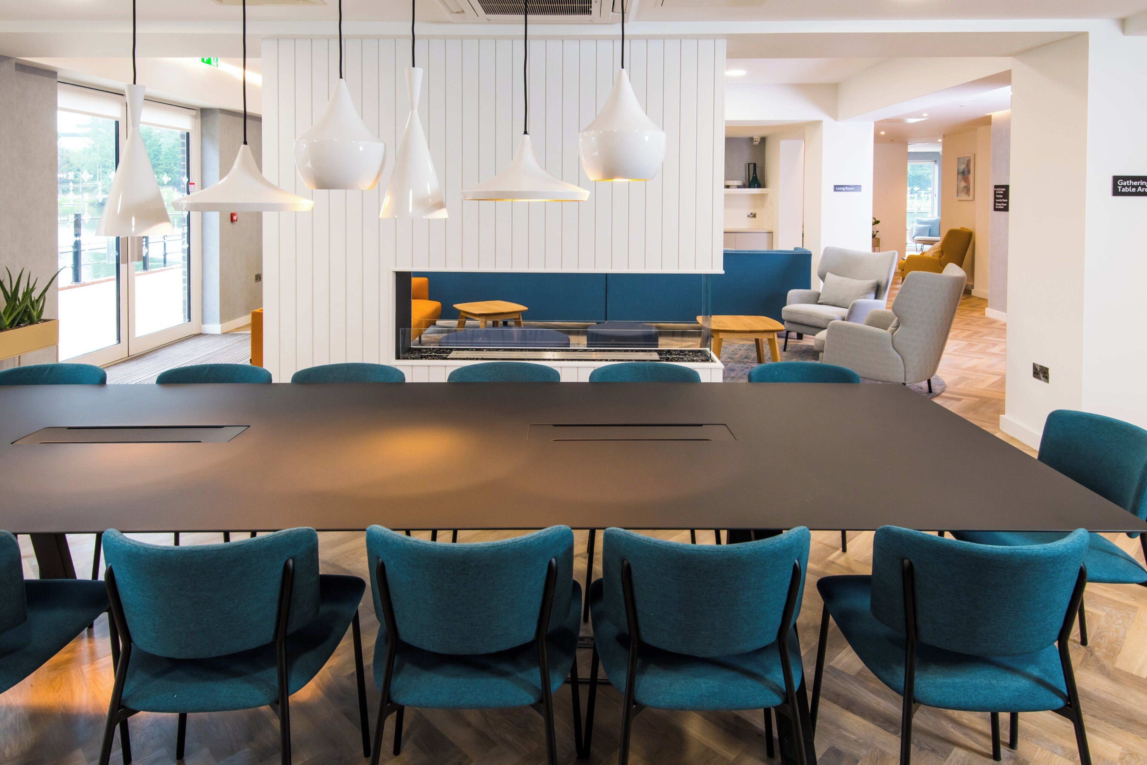 A conference room with a large table, teal chairs, and pendant lighting.
