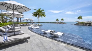 A poolside area with lounge chairs and umbrellas, a clear sky, and palm trees. - Holiday Inn Resort Ho Tram Beach by IHG (Ho Chi Minh City)