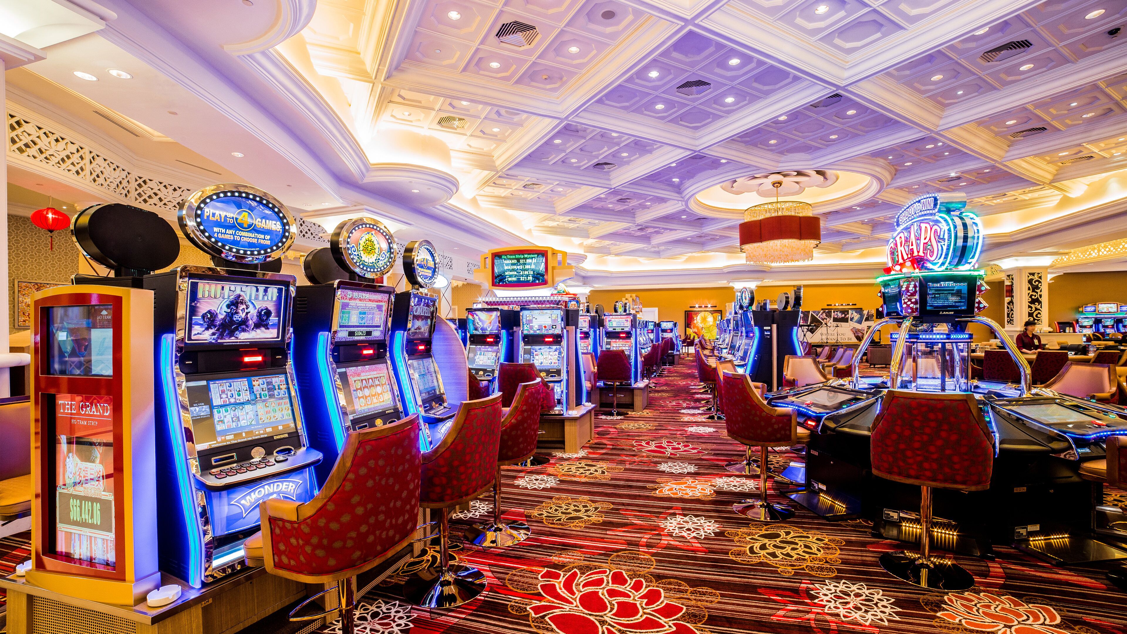 A casino with multiple slot machines and gaming tables, a patterned carpet, and a decorative ceiling.
