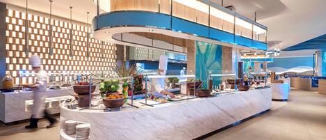 A modern hotel lobby with a marble reception desk, a kitchen area, and a decorative wall.