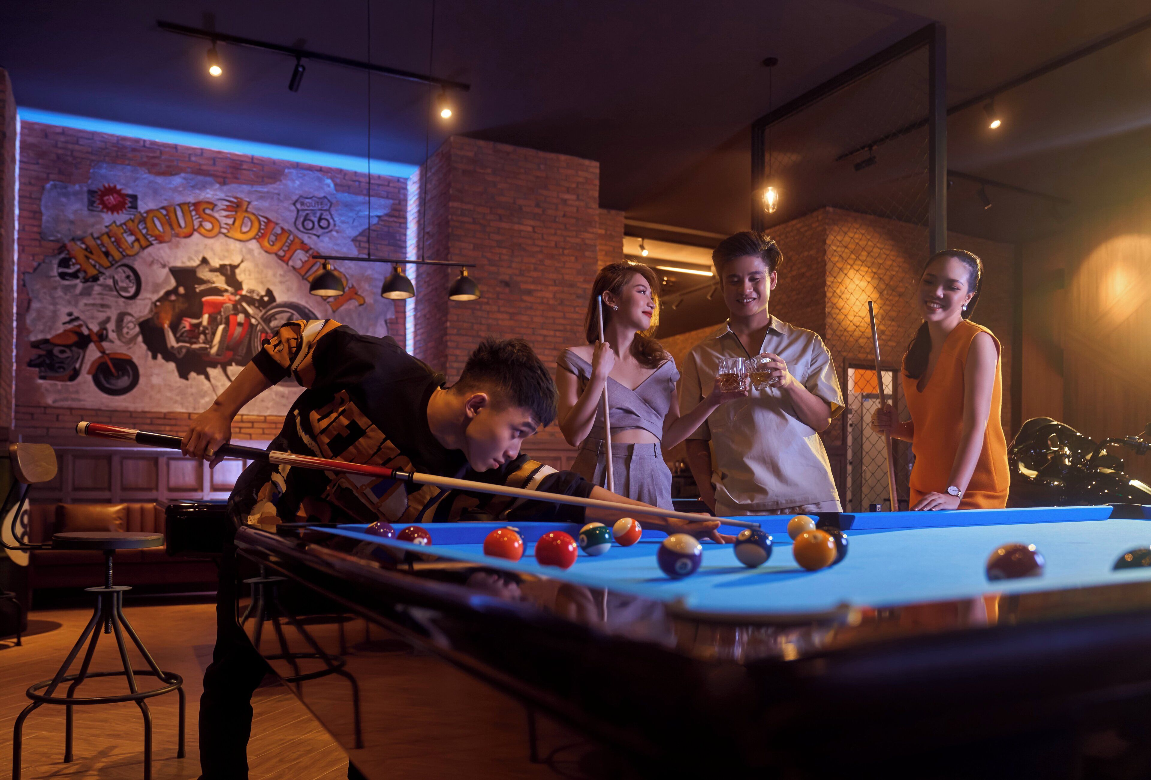 A pool table with players, a brick wall with a mural, and a bar area.