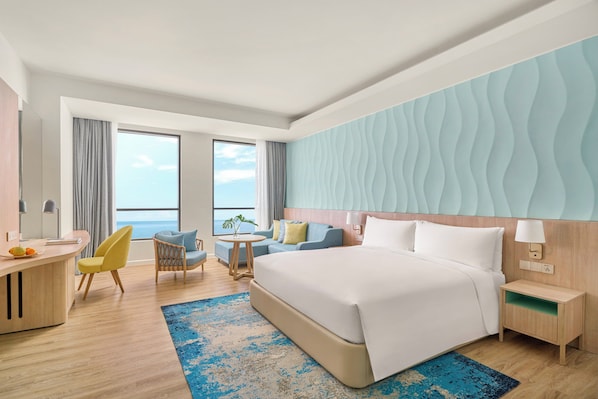 A hotel room with a large bed, a desk, a chair, a small table, and a view of the ocean. - Holiday Inn Resort Ho Tram Beach by IHG (Ho Chi Minh City)