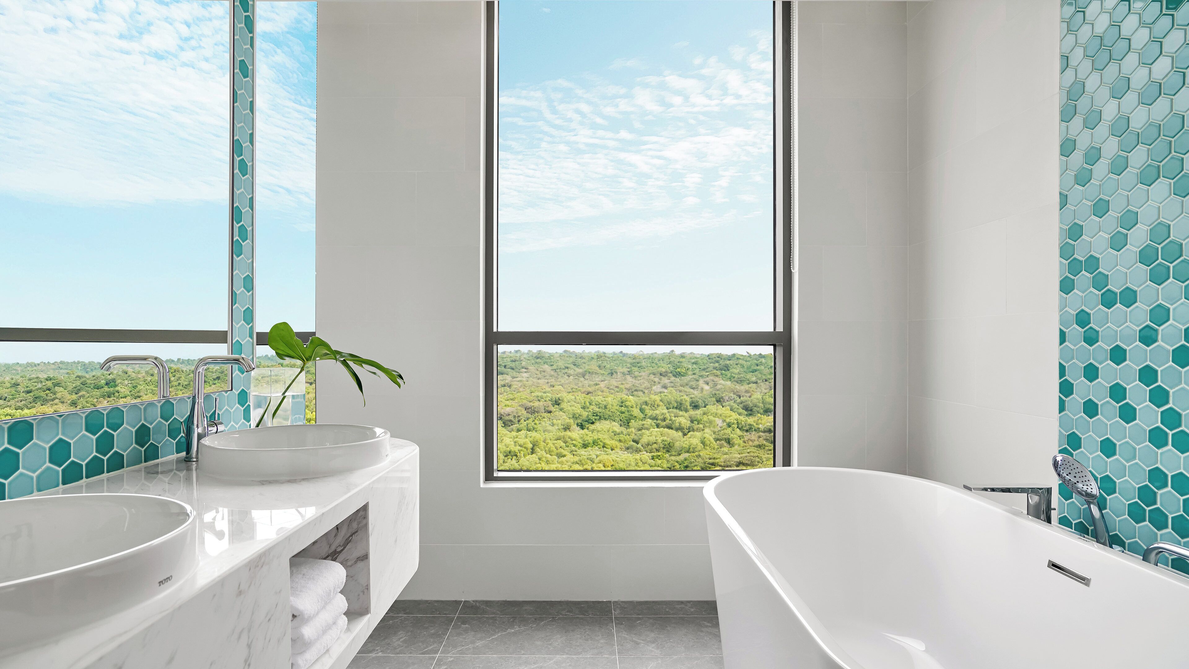 A bathroom with two sinks, a bathtub, and a large window offering a view of a green landscape.