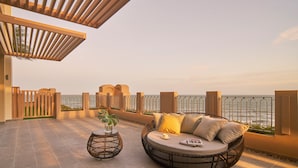 A sunlit outdoor seating area with a round wicker sofa and a small table, overlooking a body of water. - Holiday Inn Resort Ho Tram Beach by IHG (Ho Chi Minh City)