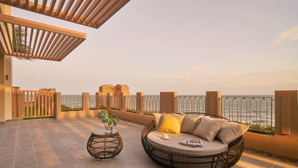 A sunlit outdoor seating area with a round wicker sofa and a small table, overlooking a body of water. - Holiday Inn Resort Ho Tram Beach by IHG (Ho Chi Minh City)