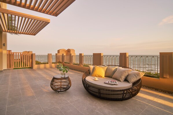 A sunlit outdoor seating area with a round wicker sofa and a small table, overlooking a body of water. - Holiday Inn Resort Ho Tram Beach by IHG (Ho Chi Minh City)