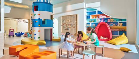 A children's play area with colorful furniture, a large blue and white play structure, and a red bean bag chair.