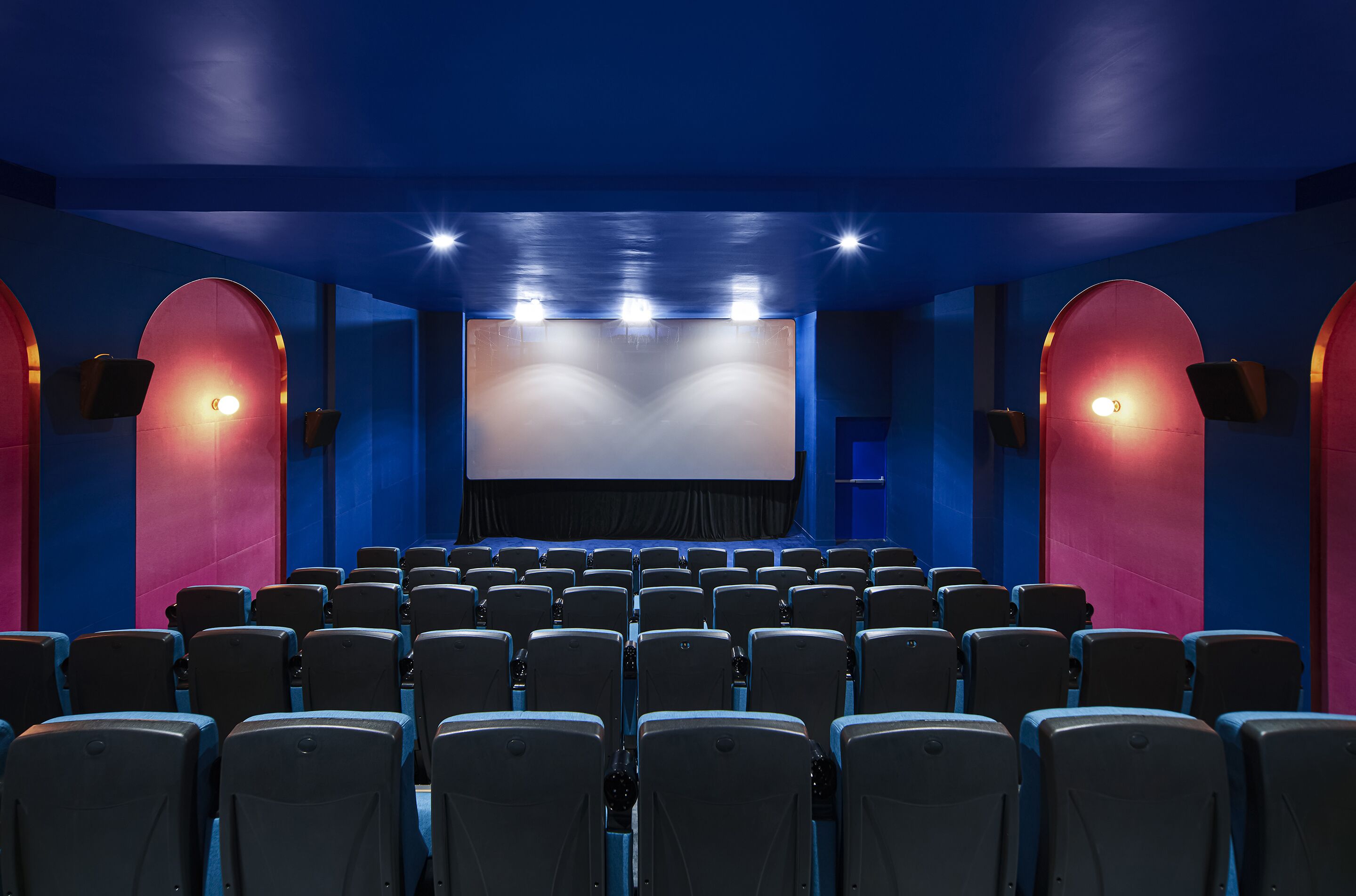 A cinema with rows of seats, a large screen, and a blue and red color scheme.