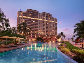 A hotel with a large pool, palm trees, and a sunset sky. - Holiday Inn Resort Ho Tram Beach by IHG (Ho Chi Minh City)