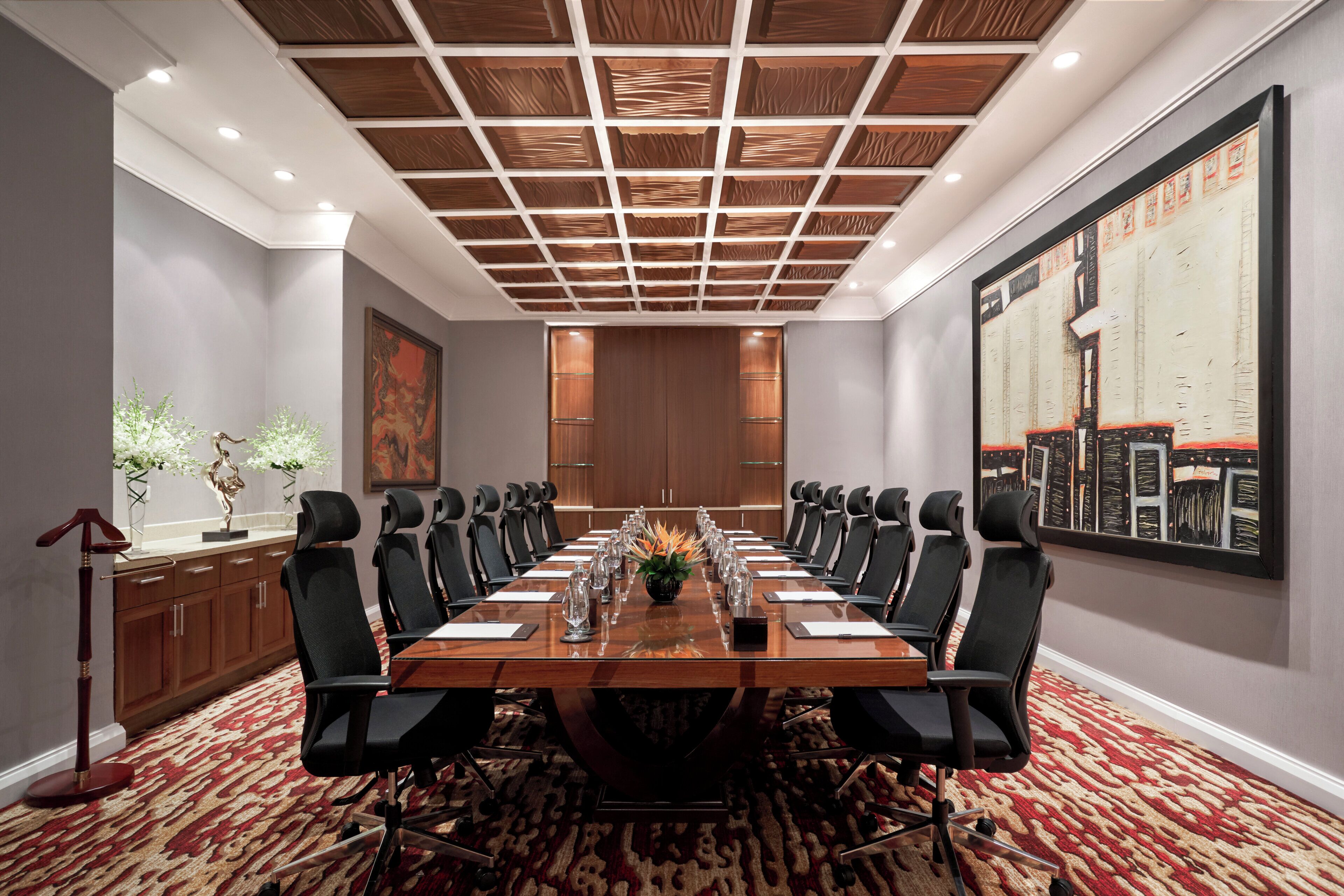 A conference room with a long table, black chairs, a wooden ceiling, and a large painting on the wall.