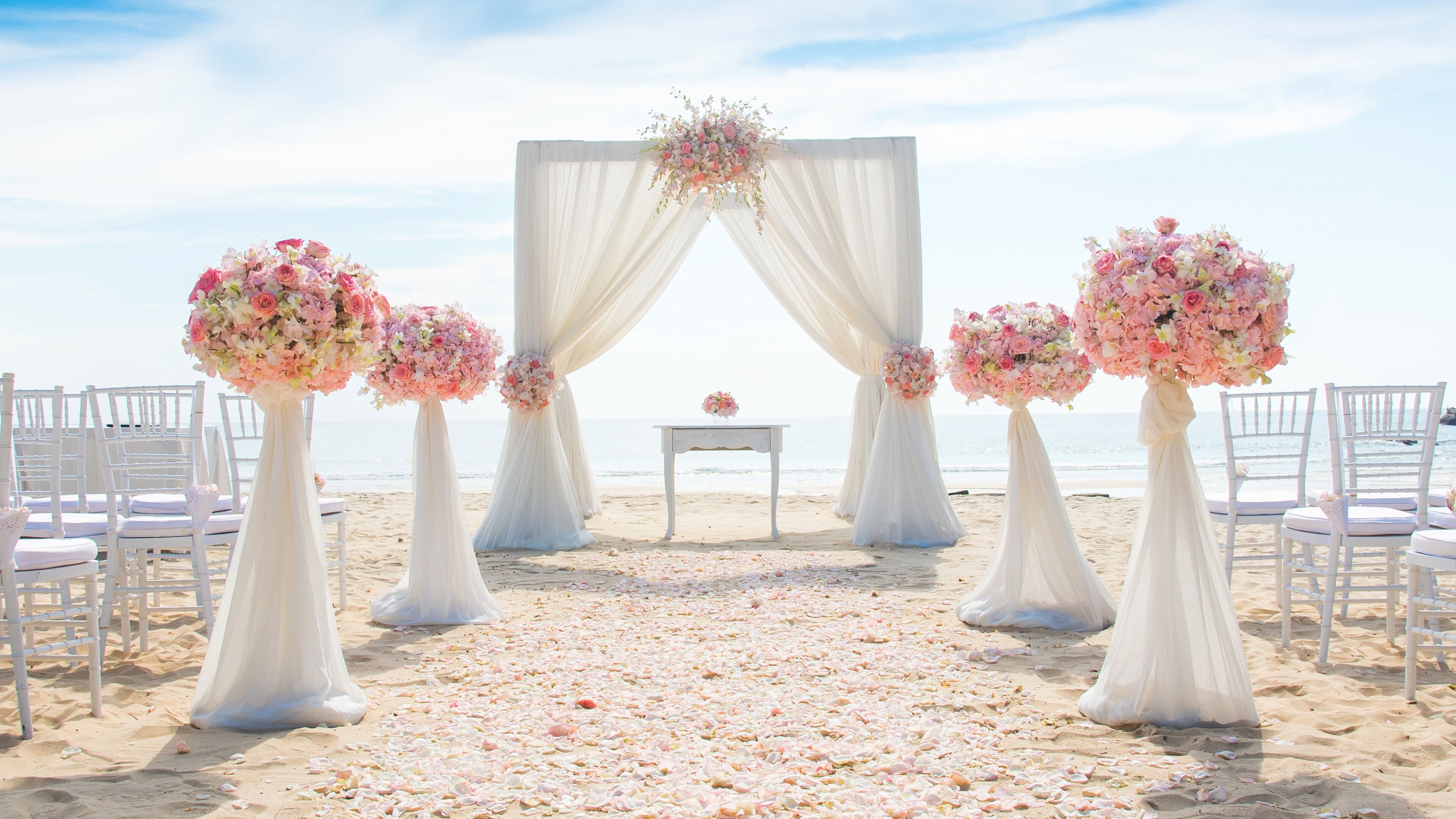 A beach wedding setup with a white altar, floral arrangements, and white chairs.