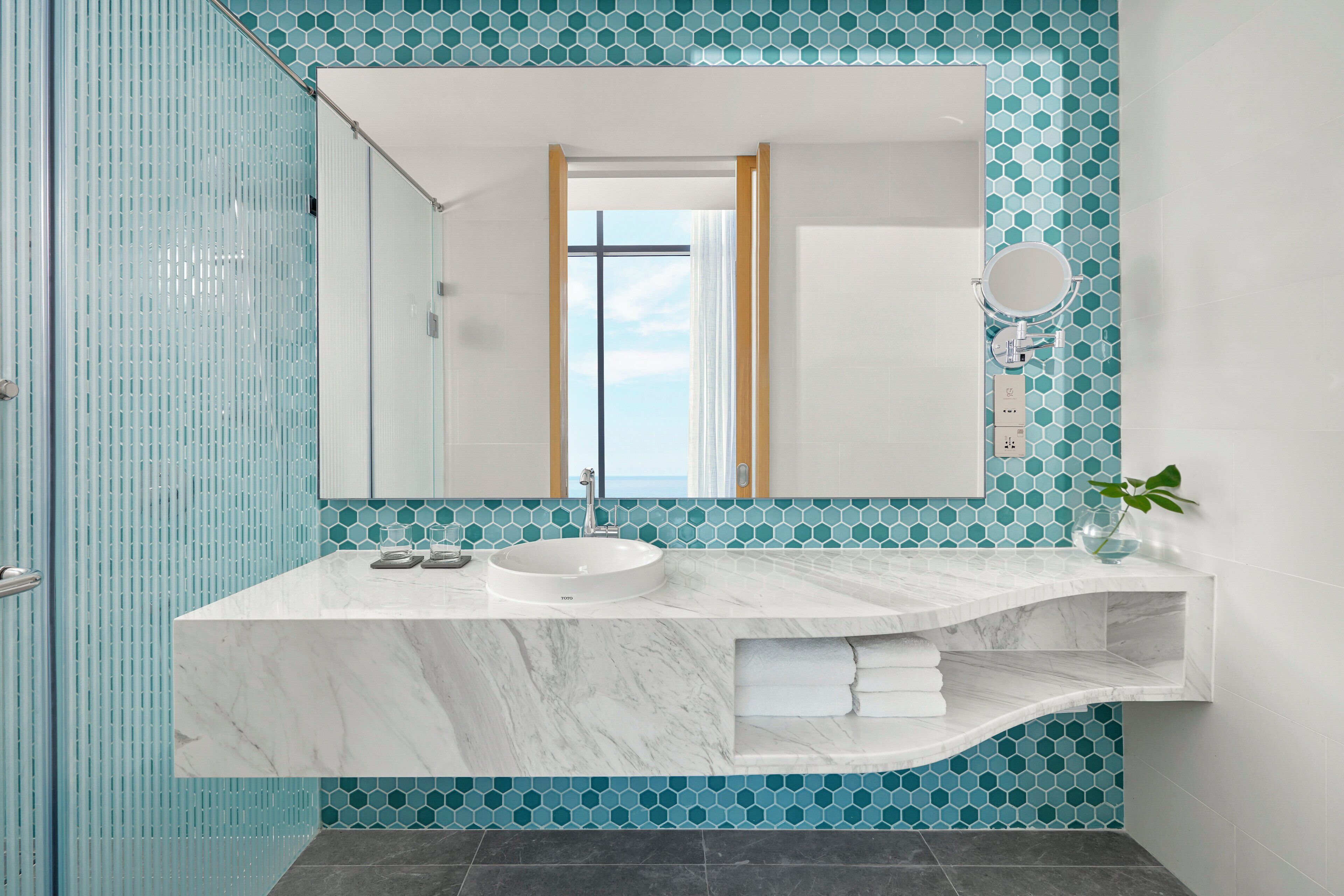 Une salle de bain avec un lavabo en marbre, un grand miroir et une vue sur la mer par une fenêtre.