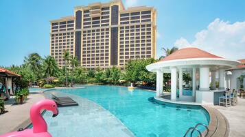 A swimming pool with a pink flamingo float, a gazebo, and a large hotel building in the background.