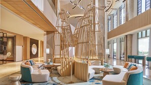 A spacious lobby with modern seating arrangements, a large wooden partition, and large windows providing natural light. - Holiday Inn Resort Ho Tram Beach by IHG (Ho Chi Minh City)