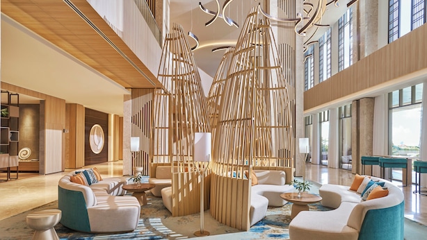 A spacious lobby with modern seating arrangements, a large wooden partition, and large windows providing natural light. - Holiday Inn Resort Ho Tram Beach by IHG (Ho Chi Minh City)