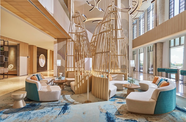 Un hall d’entrée spacieux, aménagé avec des sièges modernes, doté d’une grande cloison en bois et de larges fenêtres qui laissent entrer la lumière naturelle.
