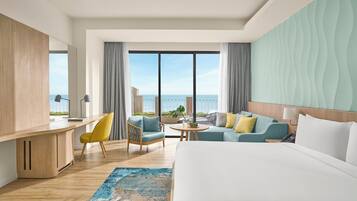 Ett hotellrum med en stor säng, ett skrivbord, en stol, en soffa och en balkong med utsikt över havet.