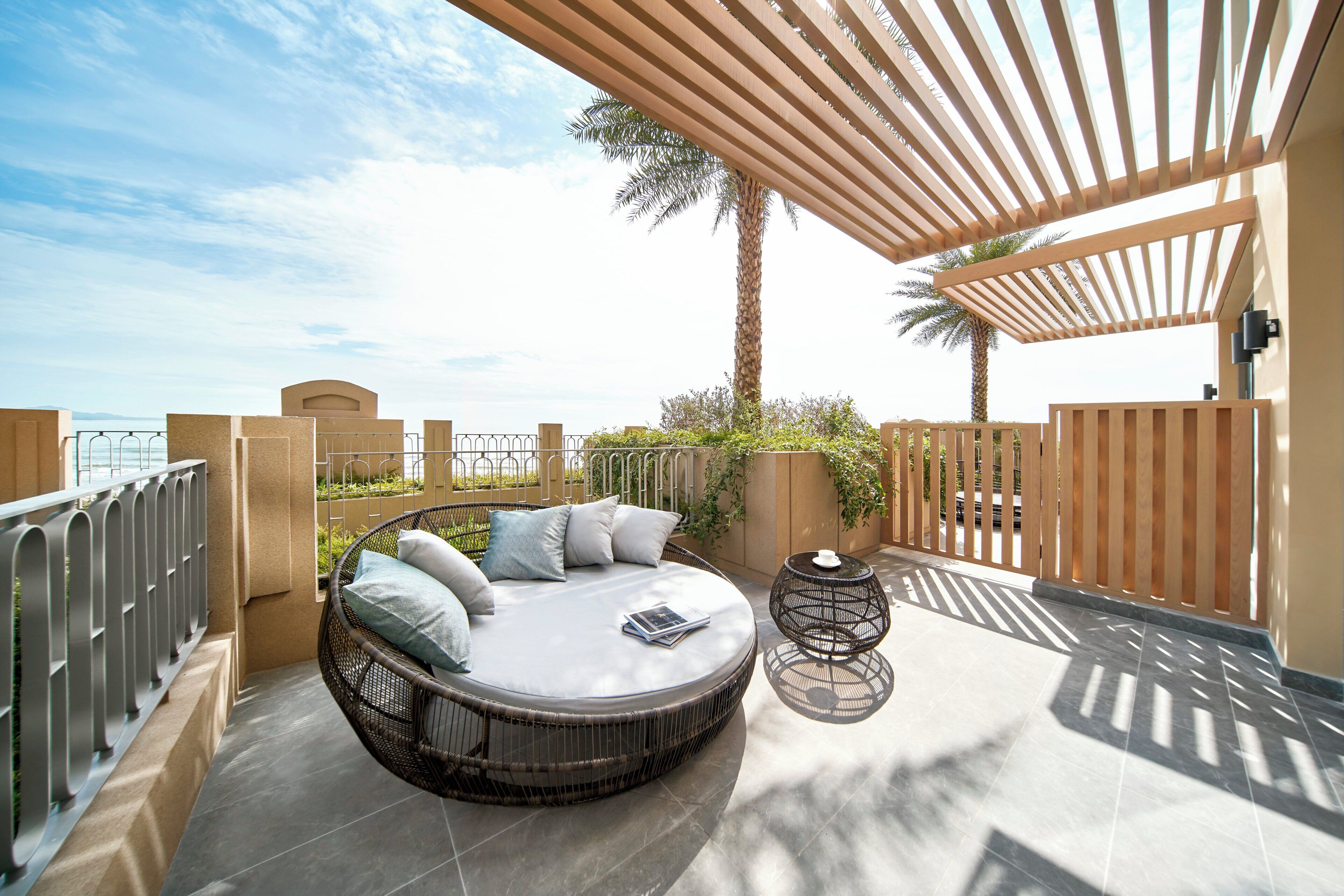 Ein sonnendurchfluteter Außenbereich mit einer runden Rattan-Couch, einem kleinen Tisch und einer Pergola.