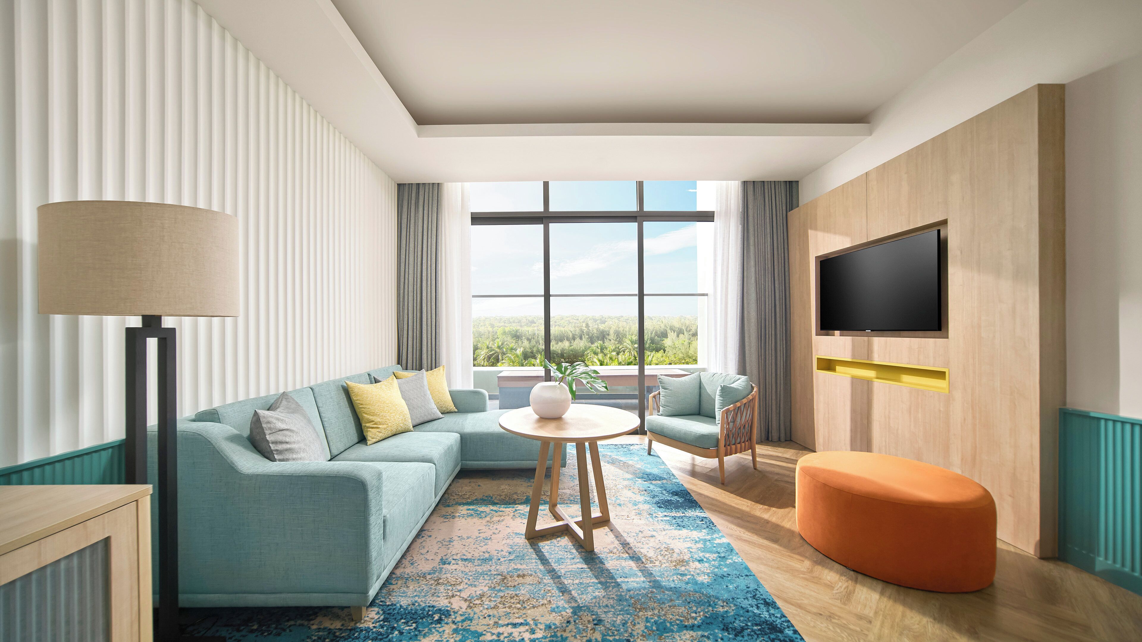 Un salon moderne comprenant un canapé, des fauteuils, une table basse, un téléviseur fixé au mur et une grande fenêtre donnant sur un paysage verdoyant.