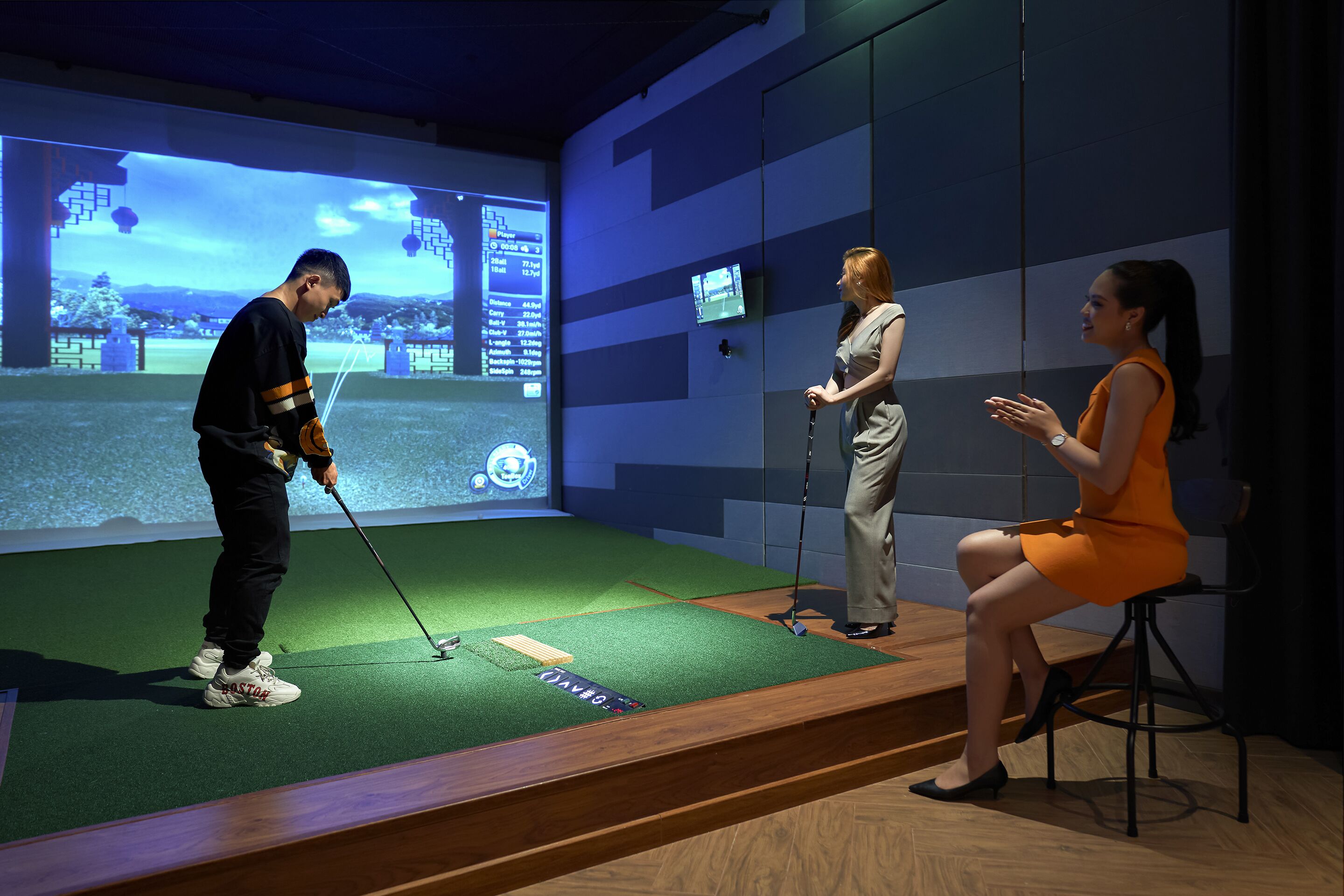 Configuração de simulação de golfe, com tela exibindo um campo de golfe, uma pessoa jogando e outra observando.