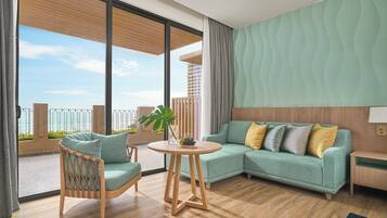 A modern living room with a sofa, a chair, a round table, and a view of the sea through large windows.
