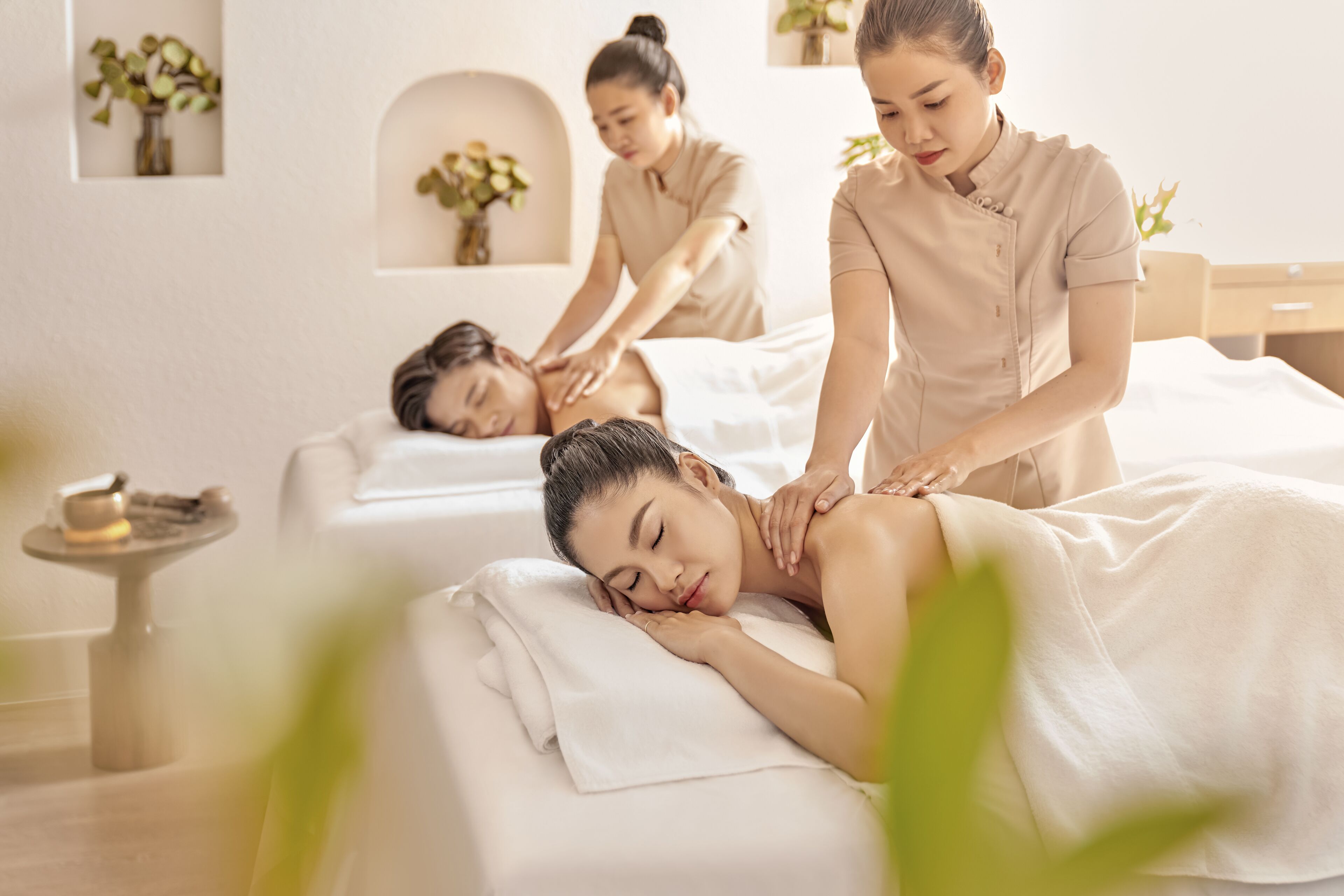 Une salle de spa équipée d’une table de massage, d’une petite table avec une bougie et d’une étagère murale agrémentée de plantes.