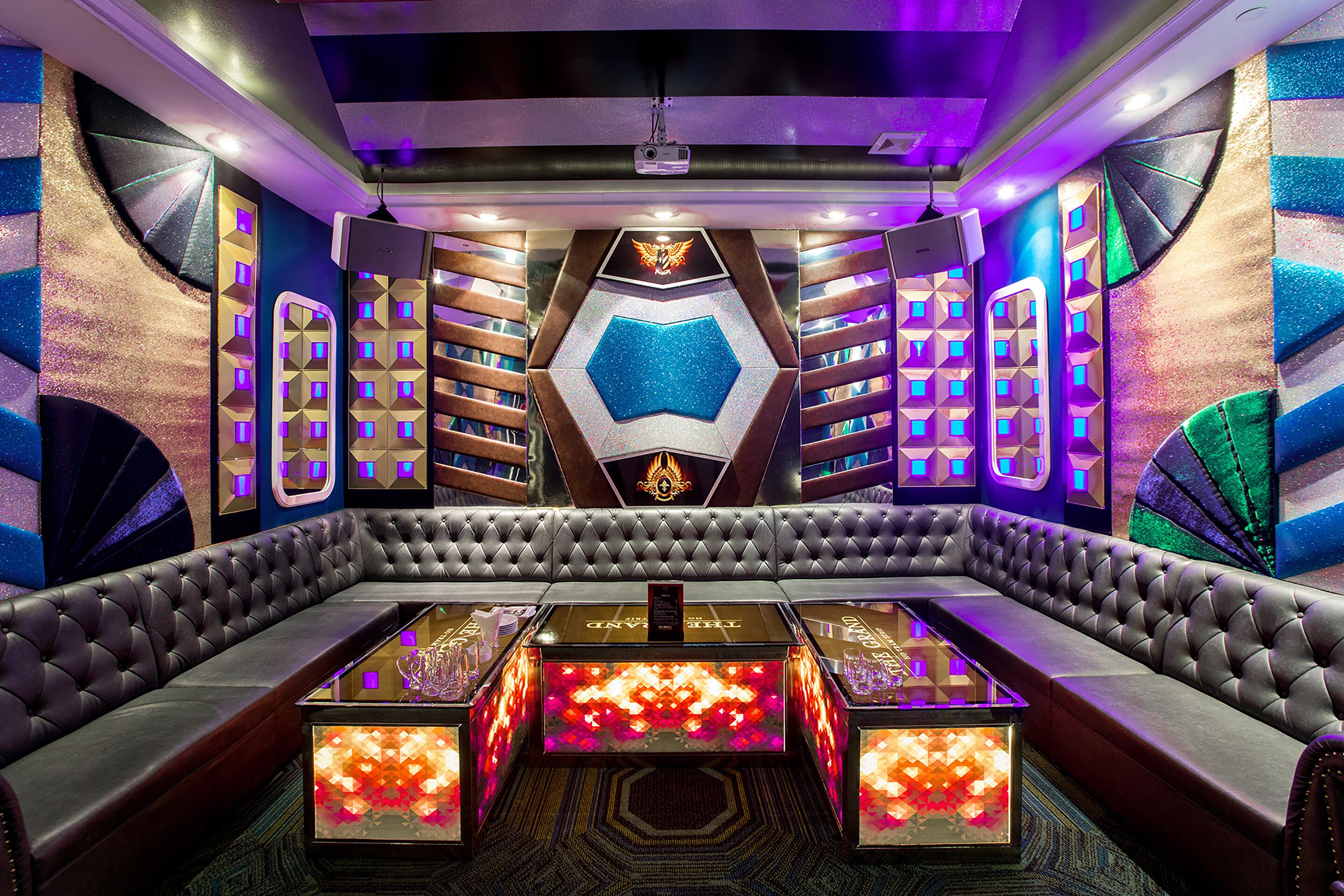 Uma área de estar luxuosa com uma mesa central, rodeada por cadeiras de encosto alto, e paredes decoradas com padrões geométricos e painéis iluminados.