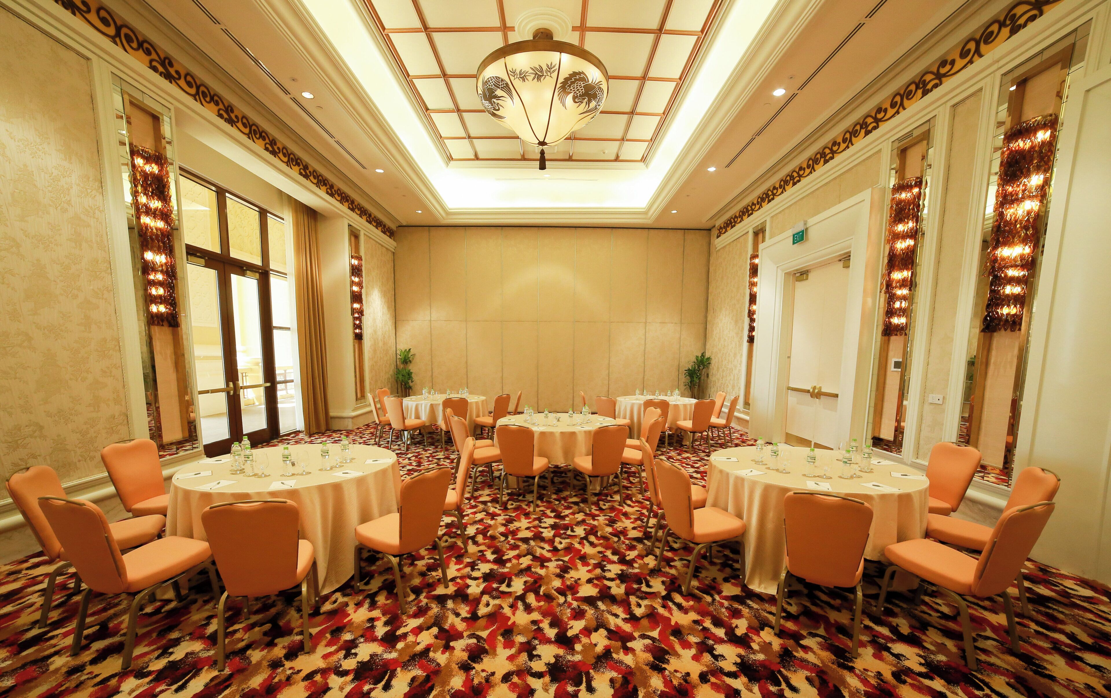 A conference room with round tables and chairs, a patterned carpet, and a decorative ceiling light.
