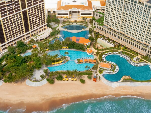 Vista aérea de un complejo turístico con múltiples piscinas, una playa y edificios de gran altura.