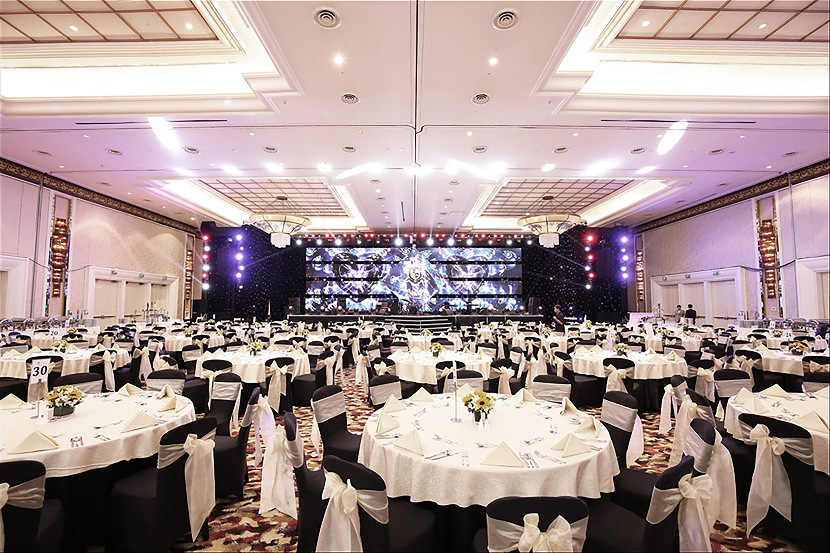 A banquet hall with round tables, black chairs, and white tablecloths.