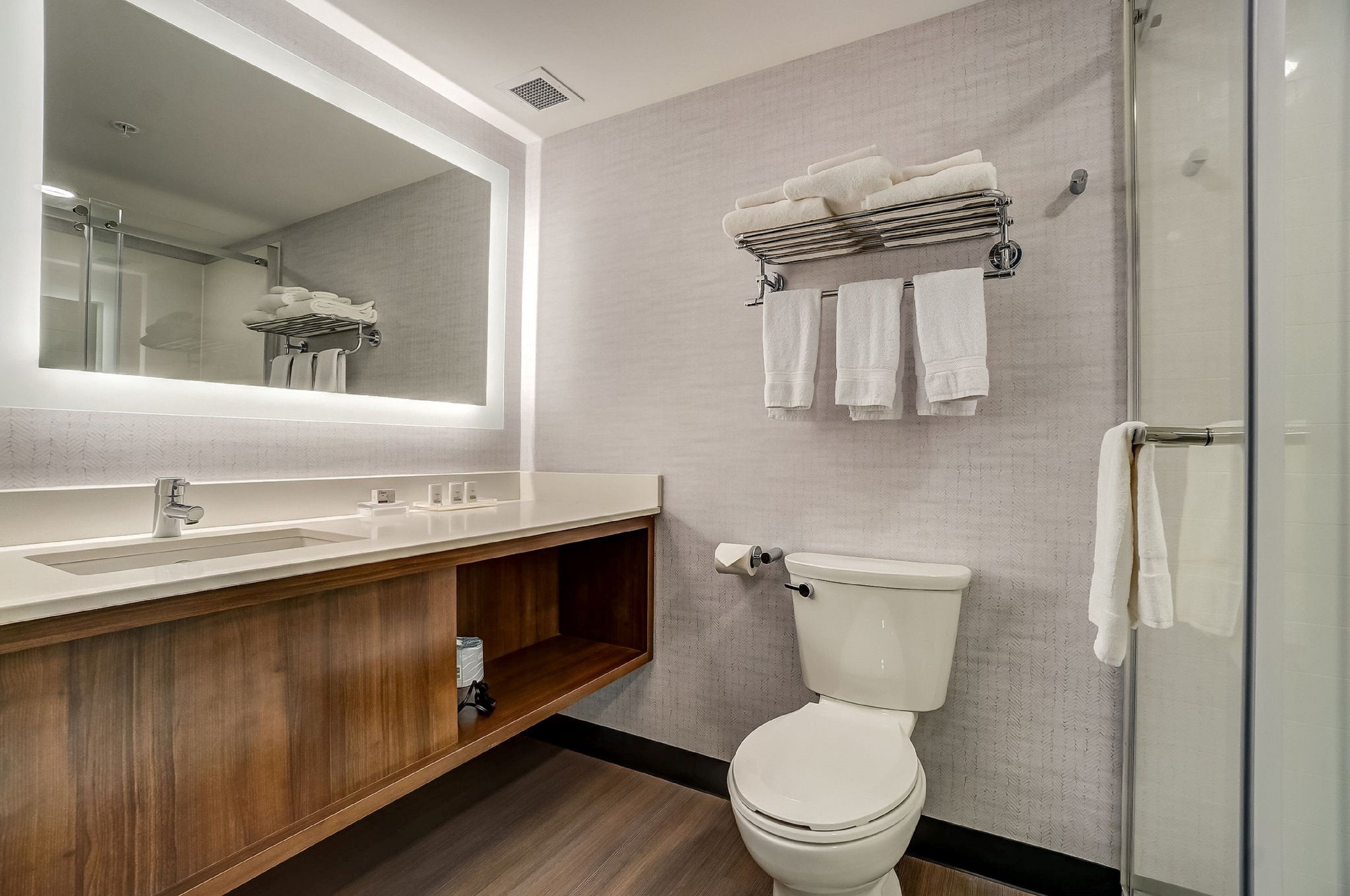 Une salle de bain moderne avec un meuble-lavabo en bois, un grand miroir, des toilettes et une cabine de douche en verre.
