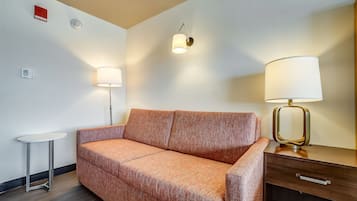 Una habitación de hotel moderna con sofá, una pequeña mesa redonda, lámpara y mesita de noche.