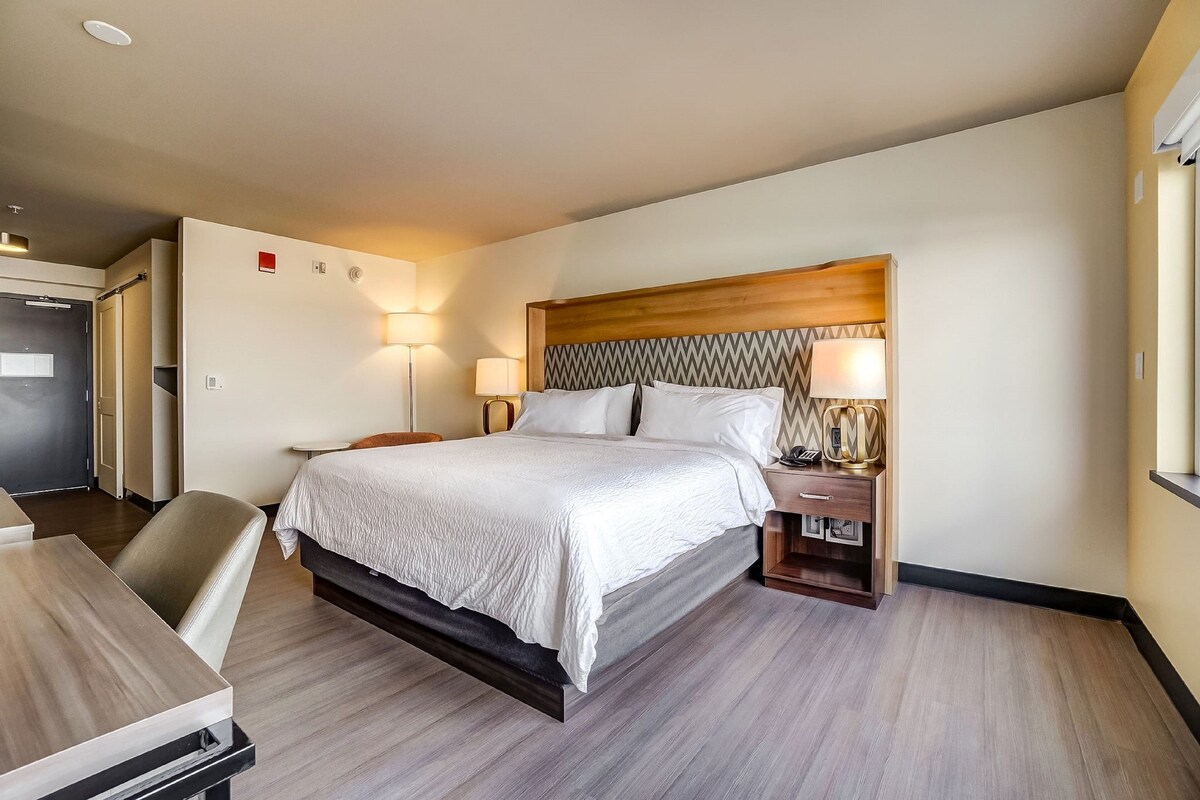 A hotel room with a bed, bedside tables, a desk, and a chair.