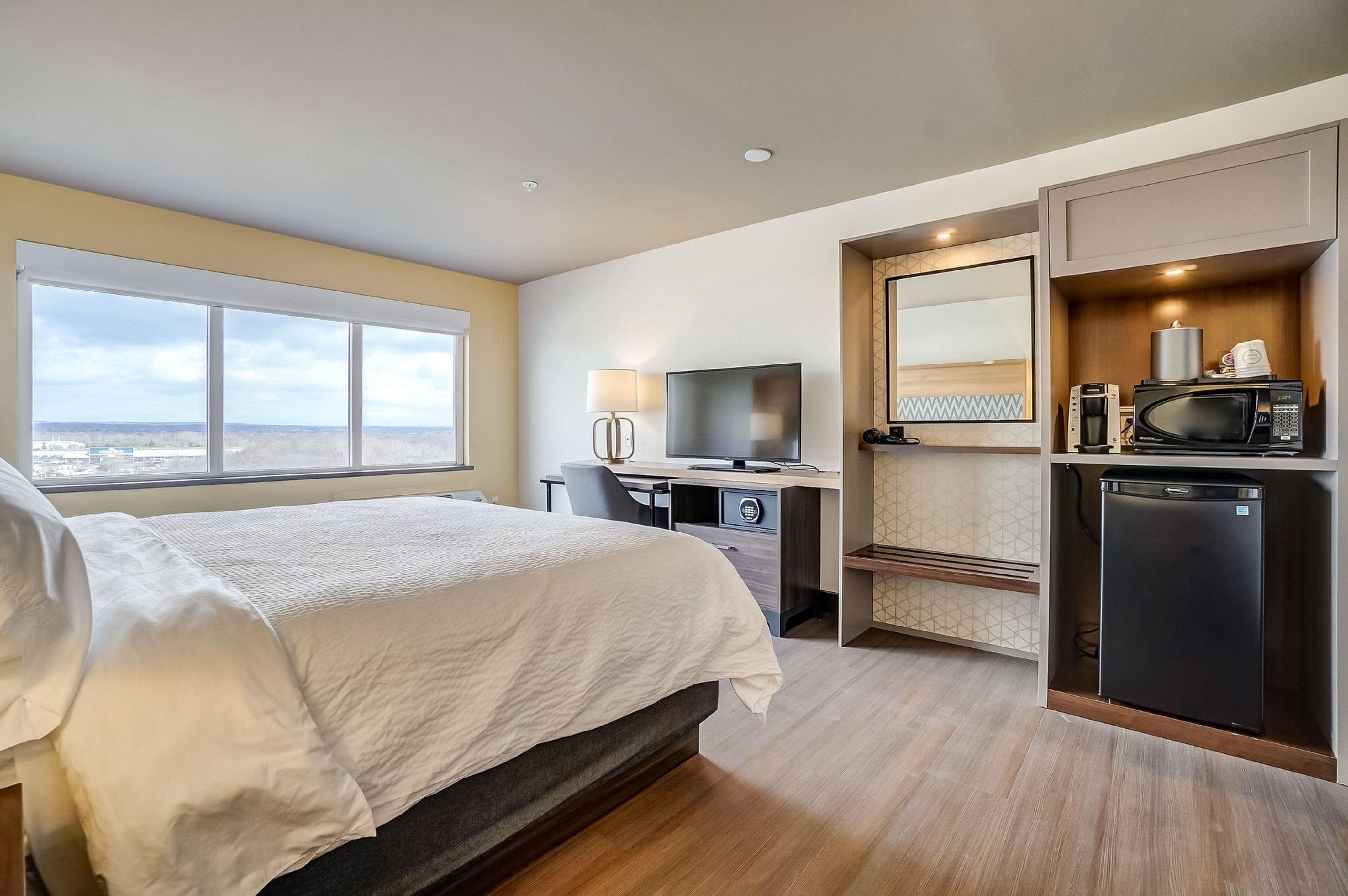 Ein Hotelzimmer mit Bett, Schreibtisch, Fernseher und einer Küchenzeile.