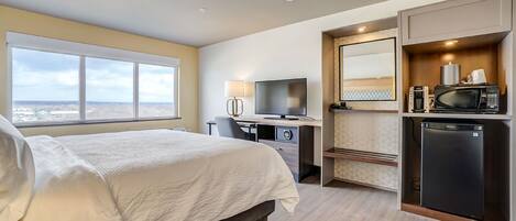 A hotel room with a bed, desk, TV, and kitchenette.