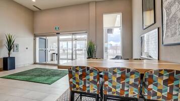A modern hotel lobby with a large wooden reception desk, patterned chairs, a green area rug, and large windows offering a view of the city.
