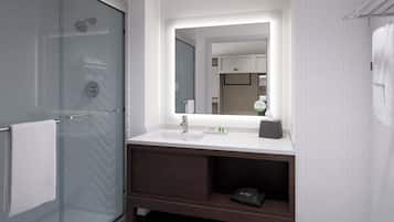Un baño moderno con cabina de ducha de vidrio, un lavamanos blanco con espejo y un mueble bajo de madera oscura.