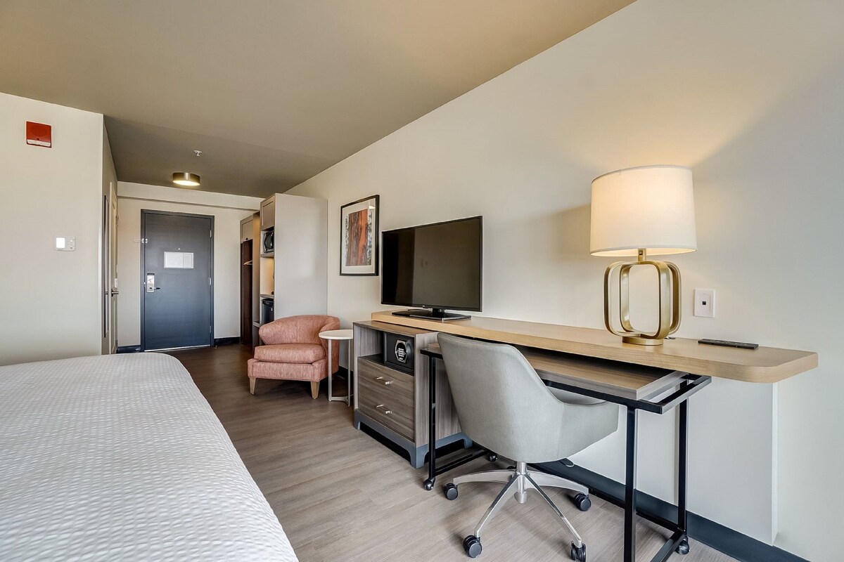 A hotel room with a bed, a desk with a computer, a chair, a lamp, and a television.