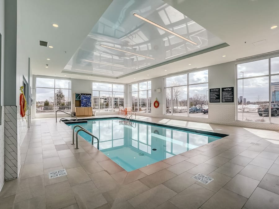 Una piscina interior moderna con paredes de vidrio transparente, ventanas amplias y suelo de baldosas.