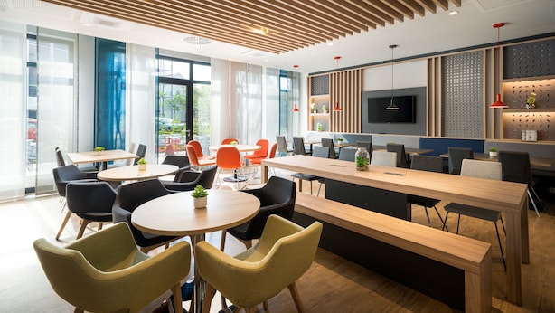 A modern office space with round tables, chairs, a long bench, and a TV mounted on the wall.