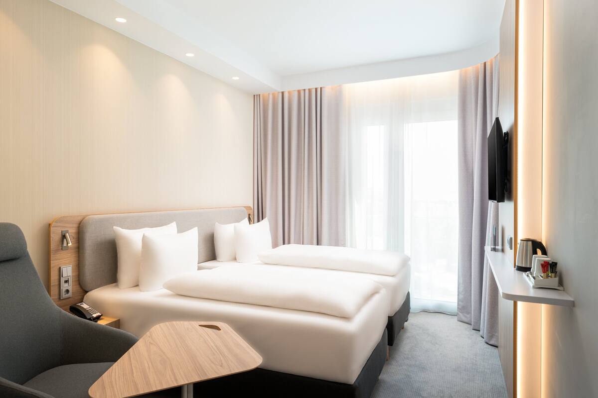 A modern hotel room with a large bed, a desk, a chair, and a flat-screen TV.