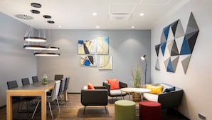 A modern meeting room with a wooden table, black chairs, a sofa, and a red ottoman.