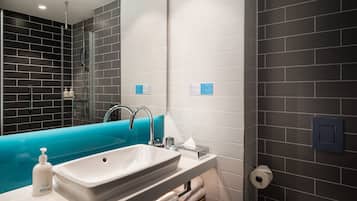 Un baño moderno con un lavamanos grande de color blanco, una bañera azul y una cabina de ducha con paredes de vidrio.