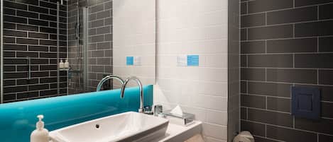 A modern bathroom with a large white sink, a blue bathtub, and a glass shower enclosure.