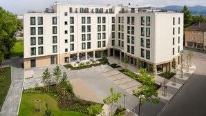 A modern multi-story hotel with a central courtyard, outdoor seating, and a parking area.