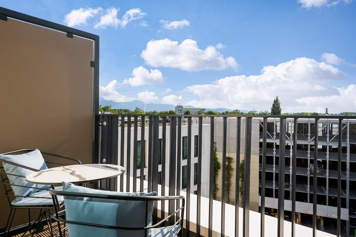 Ein Balkon mit Tisch und Stühlen, der auf eine Parkgarage und Gebäude blickt.