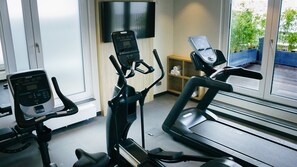 A gym with stationary bikes, a treadmill, and a TV mounted on the wall.