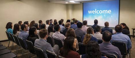 A conference room with a projector screen displaying 'welcome,' rows of chairs, and a carpeted floor.