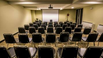 Ein Konferenzraum mit Reihen schwarzer Stühle, einer Projektionsleinwand und einer Tafel.